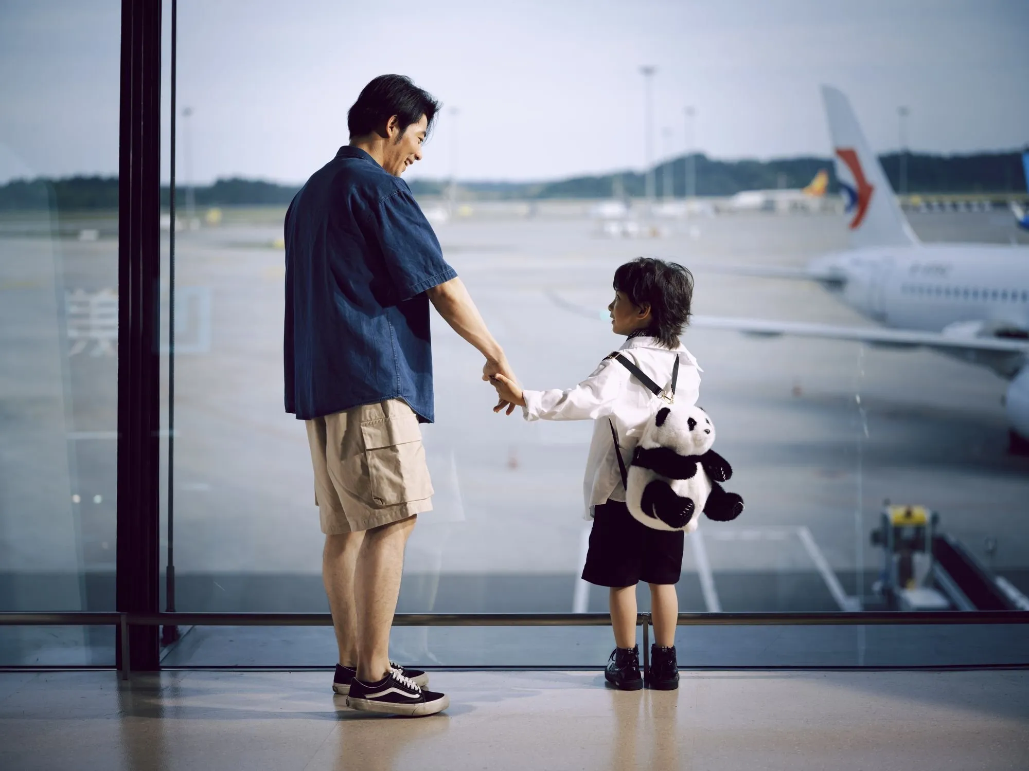 Ein Vater und sein Kind schauen im Flughafen aus dem Fenster auf die Flugzeuge